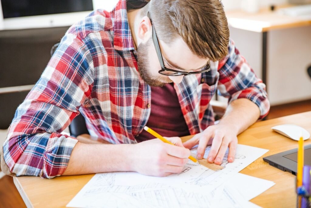 serious hardworking student sitting at the desk and drawing blueprint e1669189314638